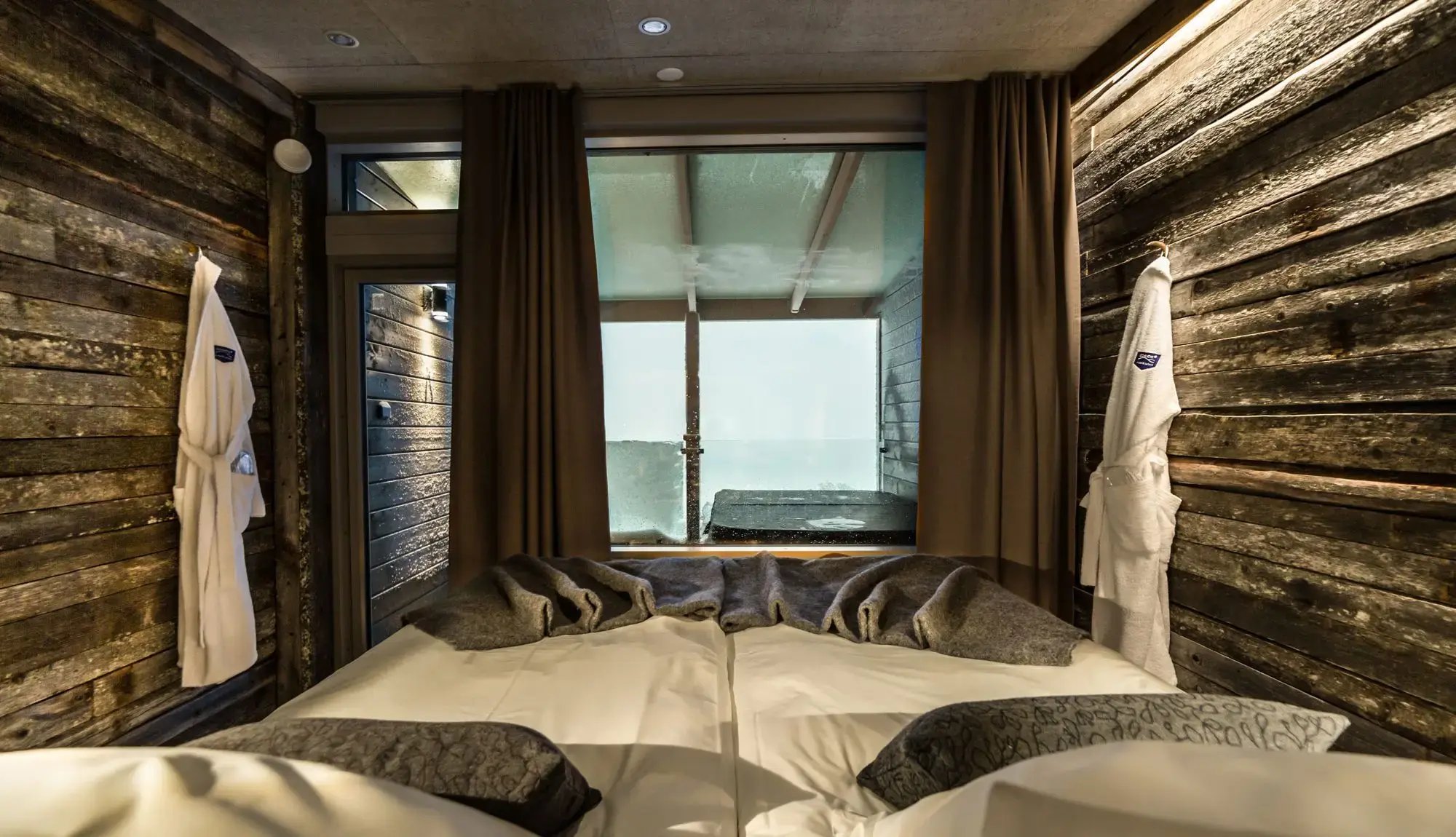 The sleeping area of the Aurora suite was raised so that the view opens out over the glass balcony fitted with a hot tub. The walls are of recycled material: old reindeer fence. The use of natural materials continues in, among other things, the lichen surfaces and the twig-branch light fittings.
