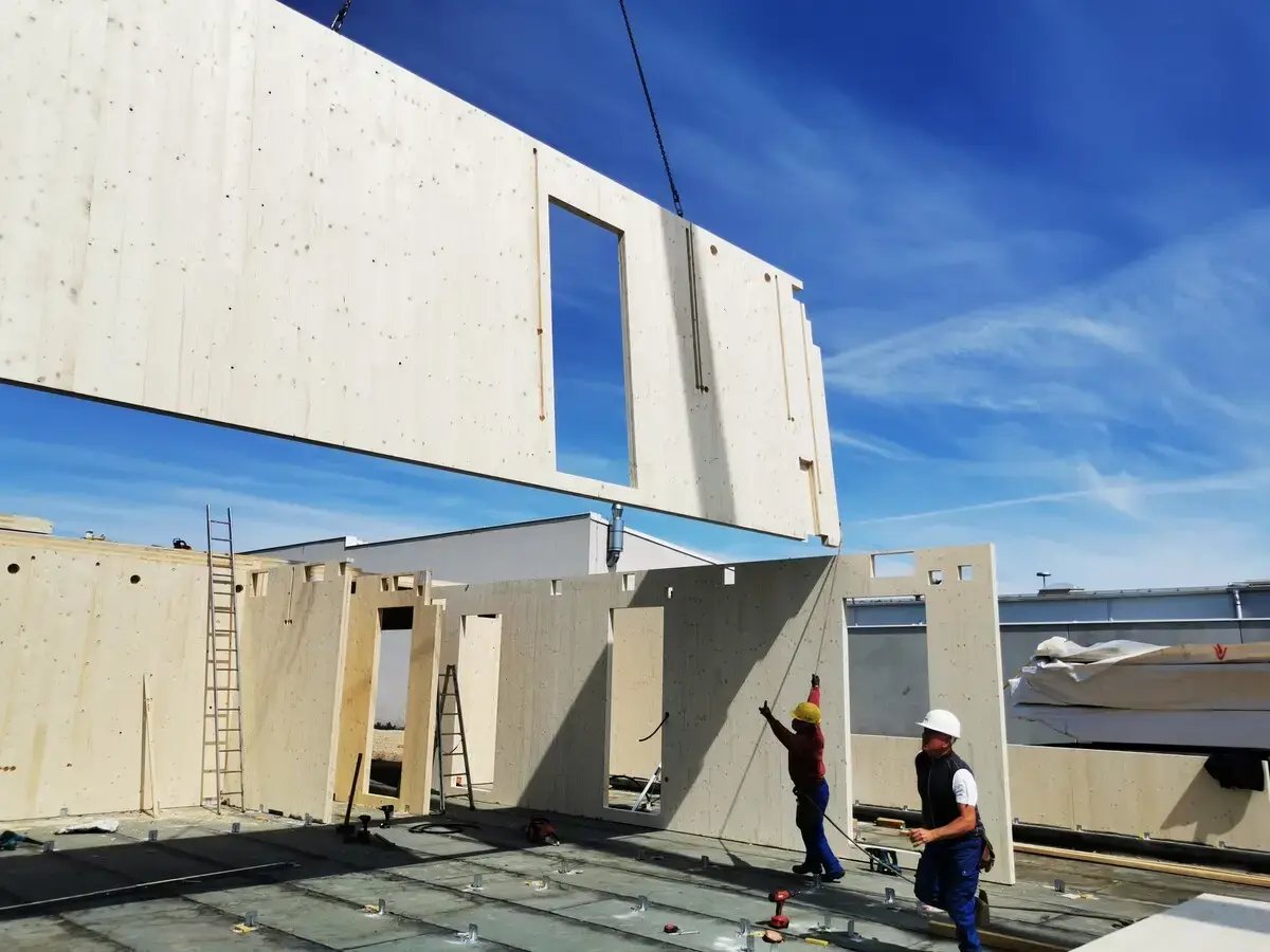 Two persons assembling a wooden wall at a construction site. 